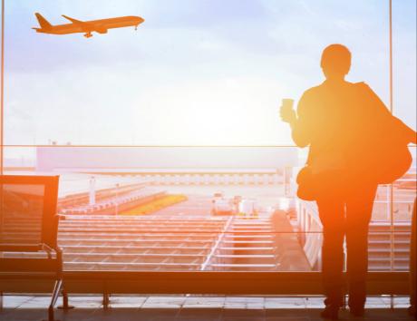 Das Bild zeigt eine Frau, die einem abhebenden Flugzeug hinterherschaut. Es dient als Illustration für eine Abreise, beispielsweise um im Ausland zu arbeiten.