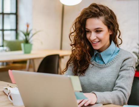 Ragazza sorridente, a mezzo busto, seduta alla scrivania di fronte a uno schermo del computer per rappresentare Curriculum senza esperienza