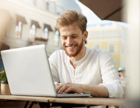 Un hombre sonriendo mirando la pantalla de su ordenador para ilustrar un currículum con perfil profesional