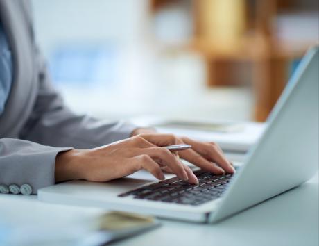 Das Bild zeigt die Hände einer Frau, die auf einer Tastatur tippen. Es dient als Illustration für die Arbeit an einem computergenerierten Lebenslauf.